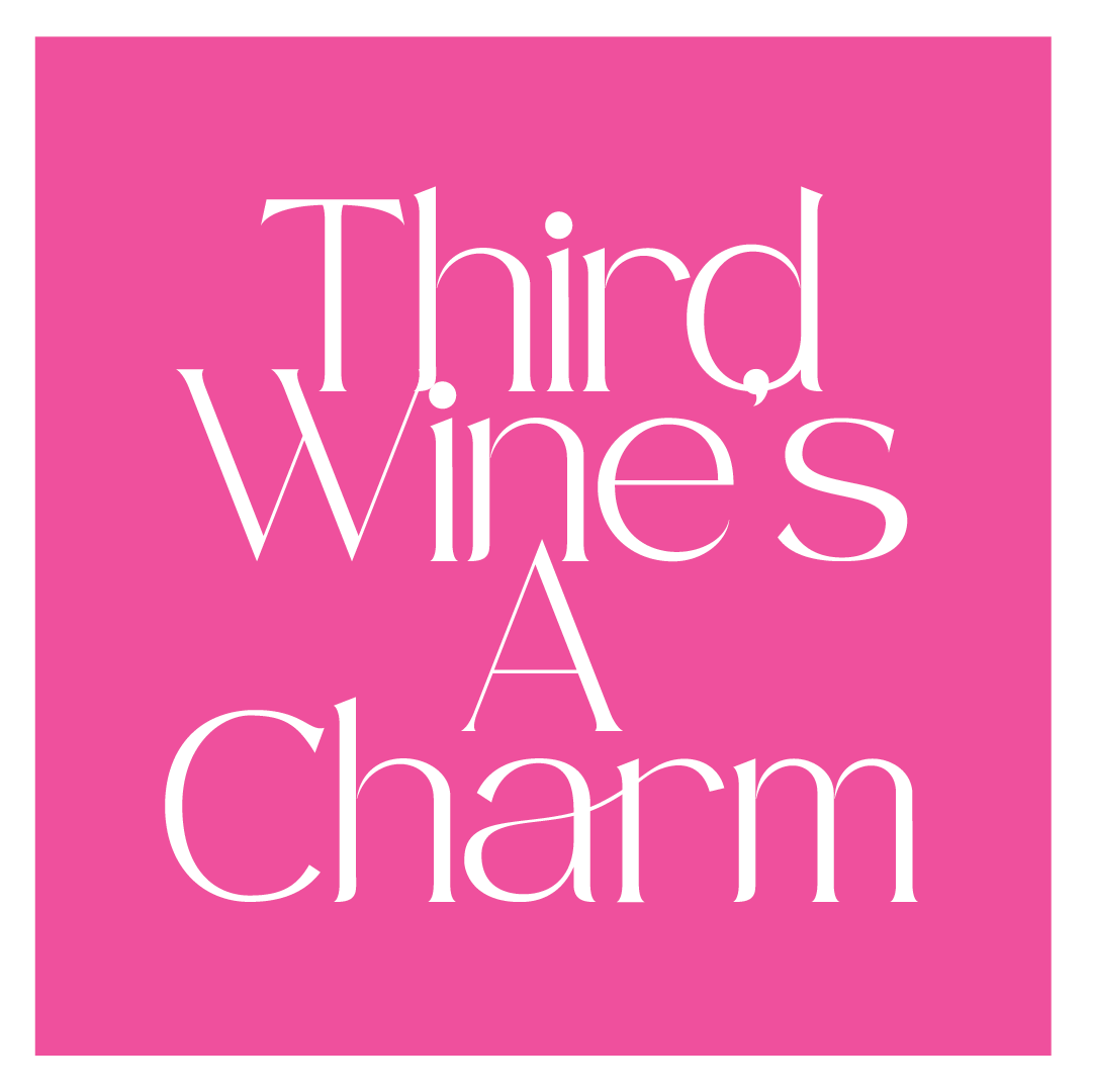 Pink cocktail napkin with white writing that says "Third Wine's A Charm"